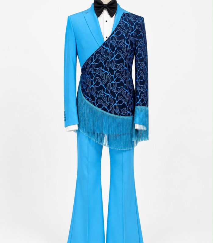 The Azure Mirage Fringe Tuxedo is a striking couture-inspired statement piece designed for gentlemen who embrace bold fashion and individuality. Crafted in a vibrant sky blue tone, this exceptional tuxedo showcases an artistic asymmetrical overlay featuring an intricate botanical pattern in deep navy and electric blue accents. The flowing fringe detail follows the sweeping diagonal design, creating movement and visual drama from every angle. Paired with matching flare-leg trousers and a classic black bow tie, this ensemble balances modern tailoring with runway-inspired creativity. Ideal for luxury weddings, red carpet appearances, stage performances, fashion events, gala evenings, and exclusive celebrations, this design is made to leave a lasting impression.